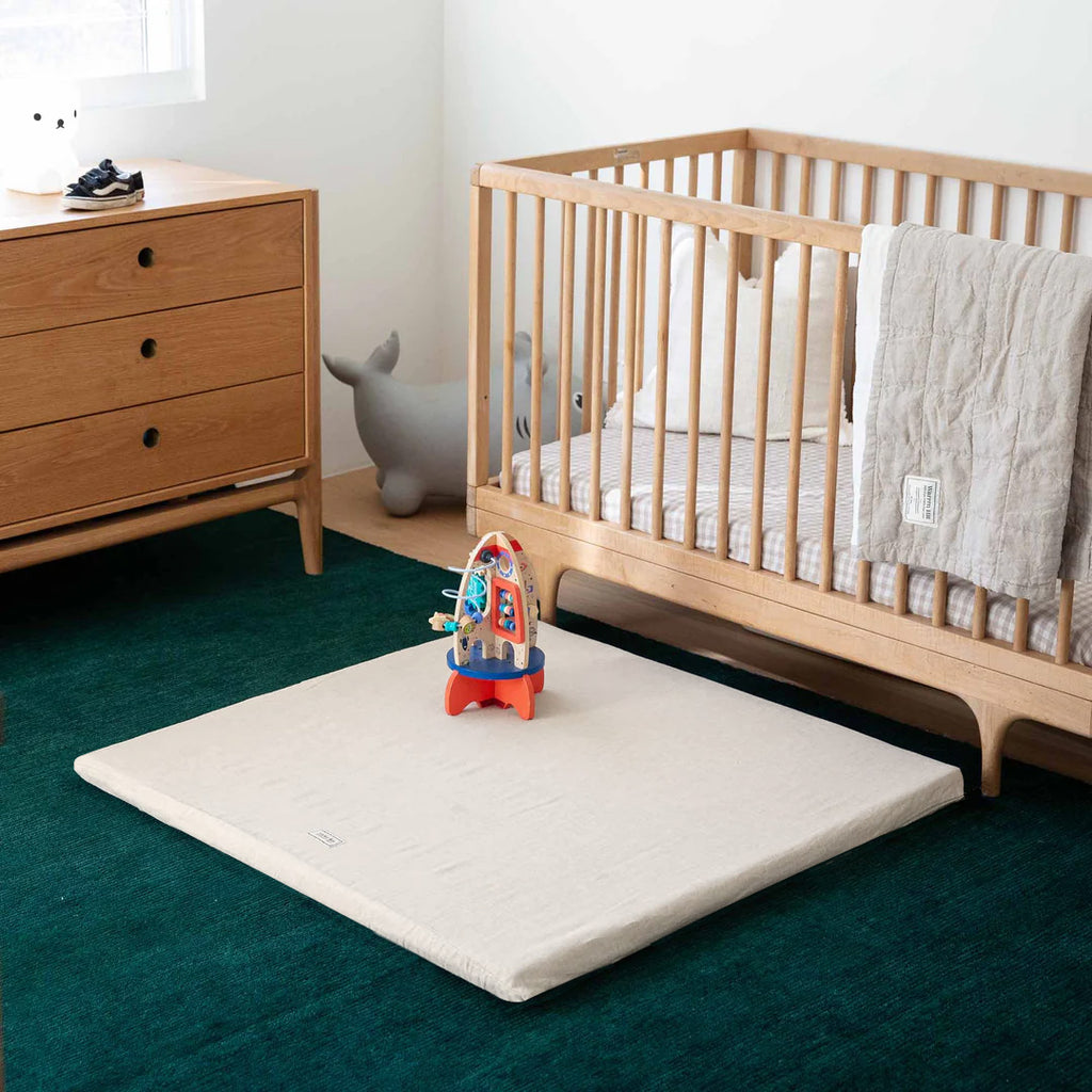 Light Natural Padded Play Mat placed in a warm-toned nursery with a wooden cot and drawers.