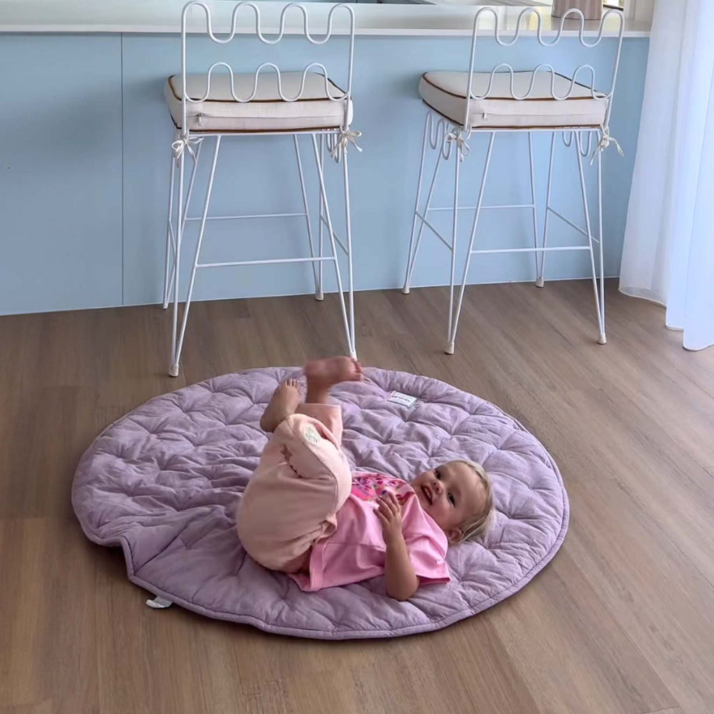 A baby lying on the Lilac Cotton Quilted Play Mat in a modern home interior.