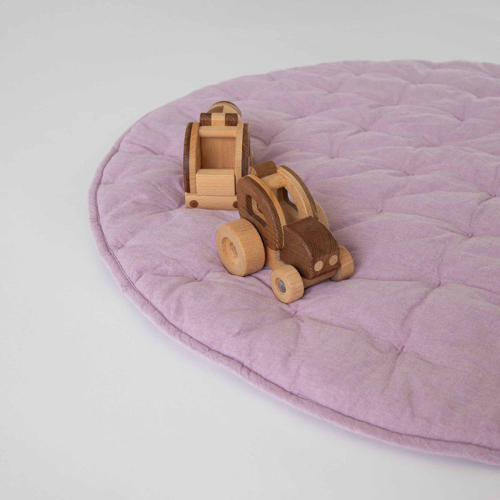 Side view of the Lilac Cotton Quilted Play Mat with wooden toy trucks on top.