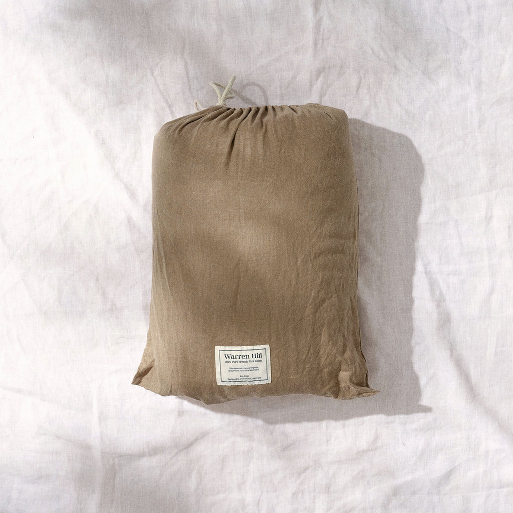 The Warren Hill Olive Husk Quilted Linen Play Mat inside its linen dust bag