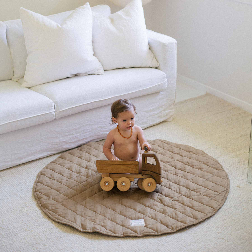 A neutral-toned room featuring the Olive Husk Quilted Linen Play Mat as a centrepiece