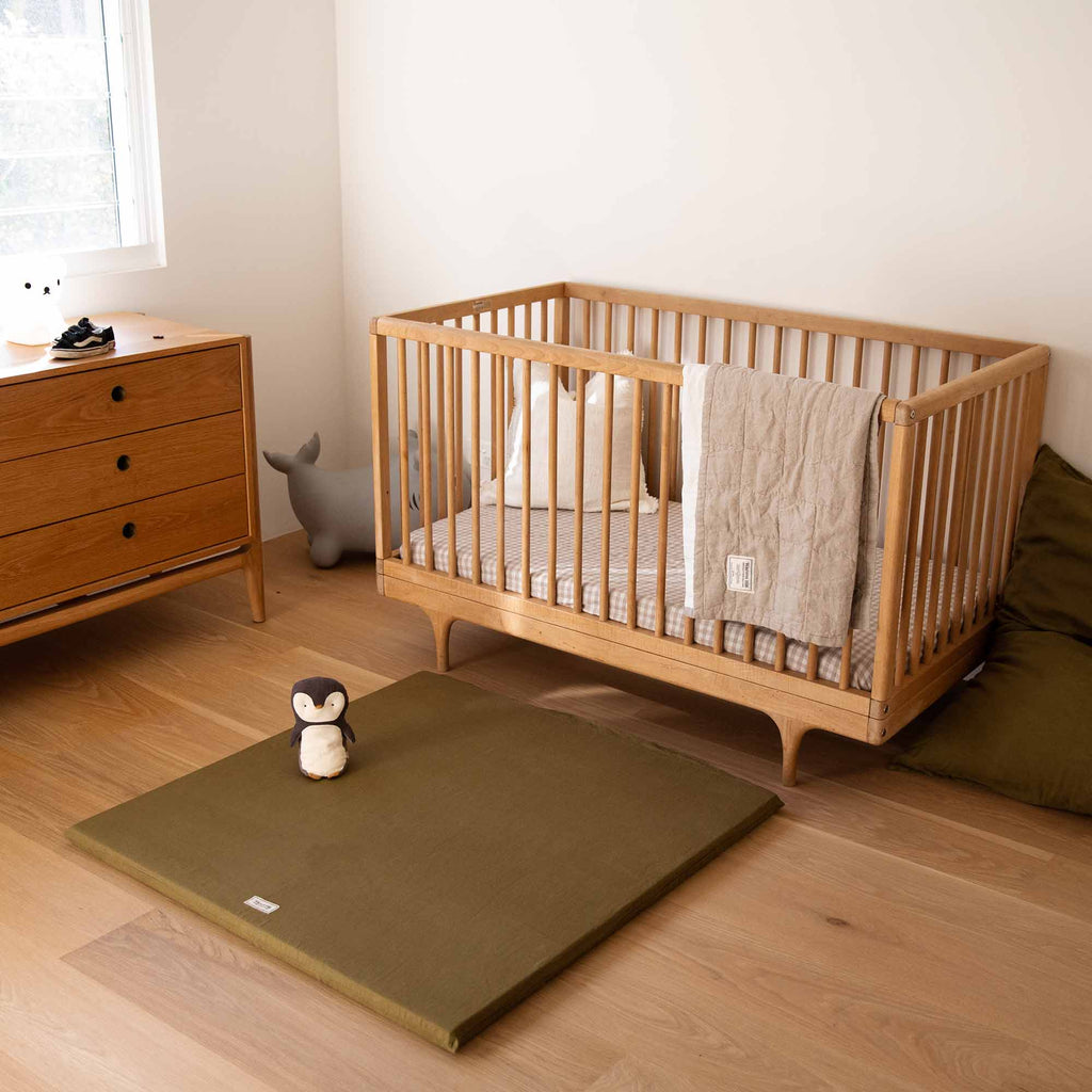 Olive Padded Play Mat placed in a warm-toned nursery with a wooden cot and drawers.