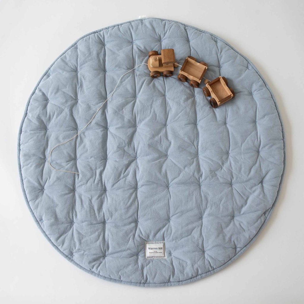 Sky Blue Cotton Quilted Play Mat by Warren Hill laid flat with wooden toy trucks on top