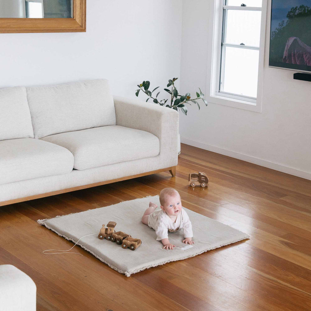 A baby enjoying tummy time on the Linen Padded Play Mat – Raw Edge in a modern living room.