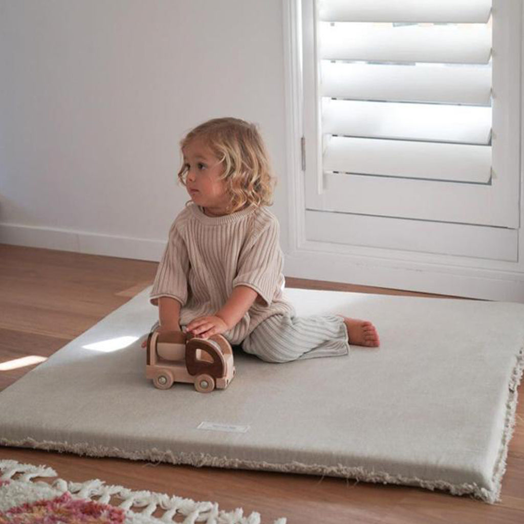 A toddler exploring the Linen Padded Play Mat – Raw Edge in a neutral-toned nursery.