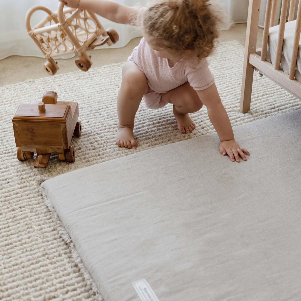 A toddler next to the Linen Padded Play Mat – Raw Edge while playing with a wooden toy.