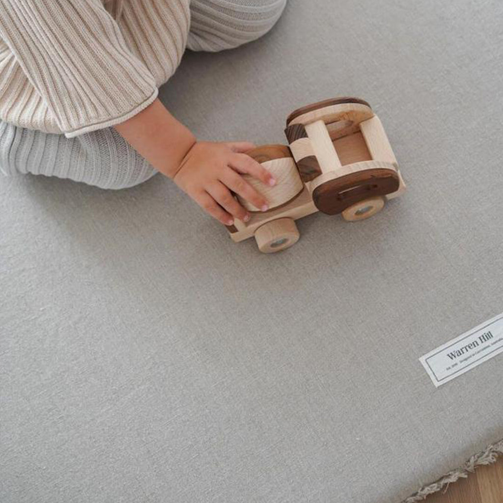 A toddler sitting on the Linen Padded Play Mat – Raw Edge while playing with a wooden toy.