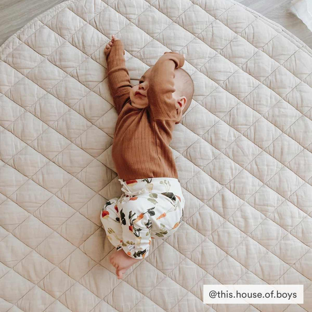 Baby stretching on a soft, quilted linen play mat in Natural colour