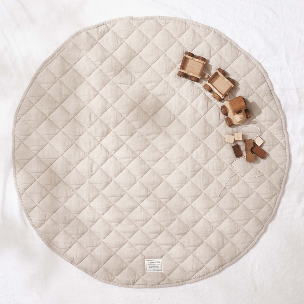 Flat lay of a folded Natural Quilted Linen Play Mat with baby essentials