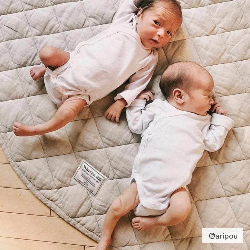 Two babies laying on a soft, quilted linen play mat in Natural colour